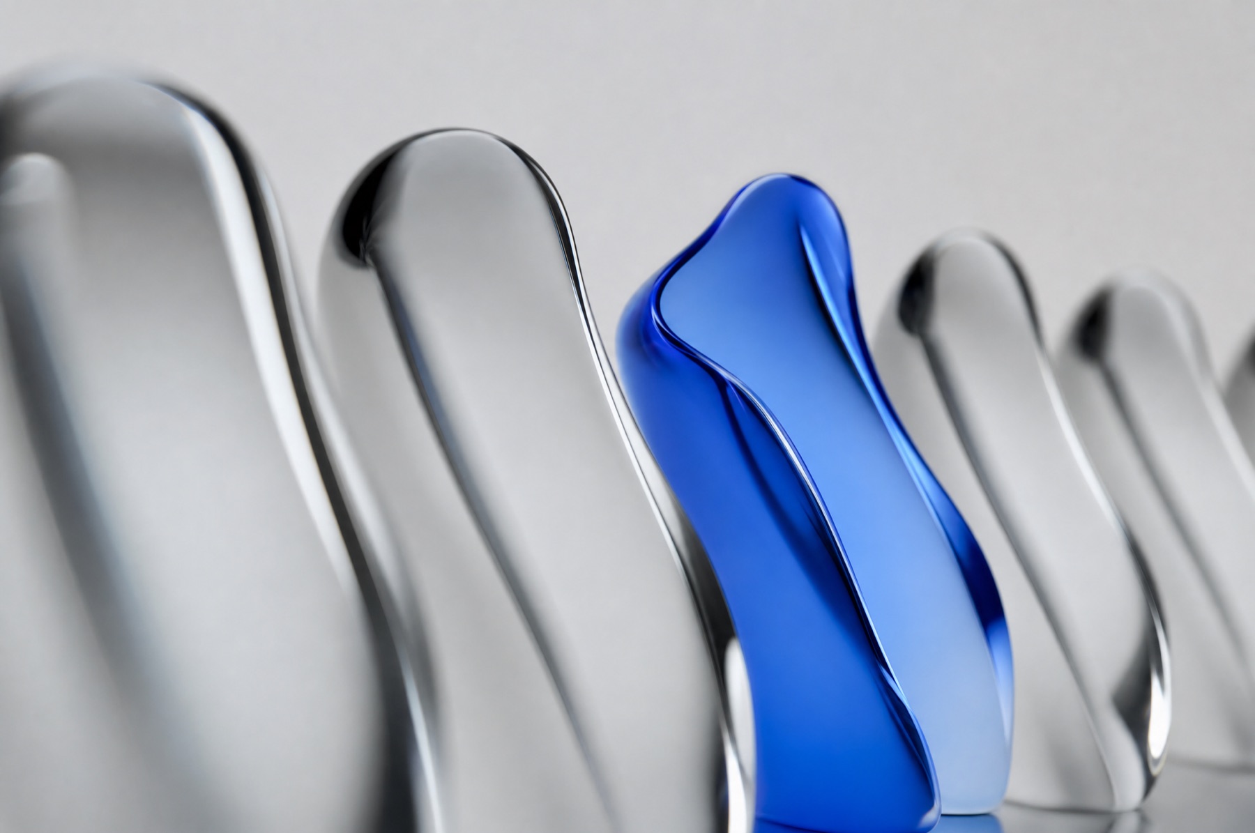 Mehrere fast gleiche graue Glasformen stehen in einer Reihe, eine einzelne blaue weicht leicht ab, als Sinnbild für eine Vorgabe, die jeder anders liest.
